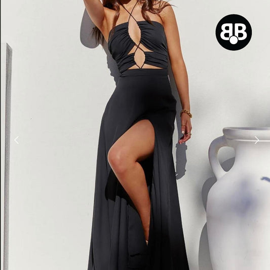 Woman wearing a black dress with cut-out design and slit, standing against a white background.