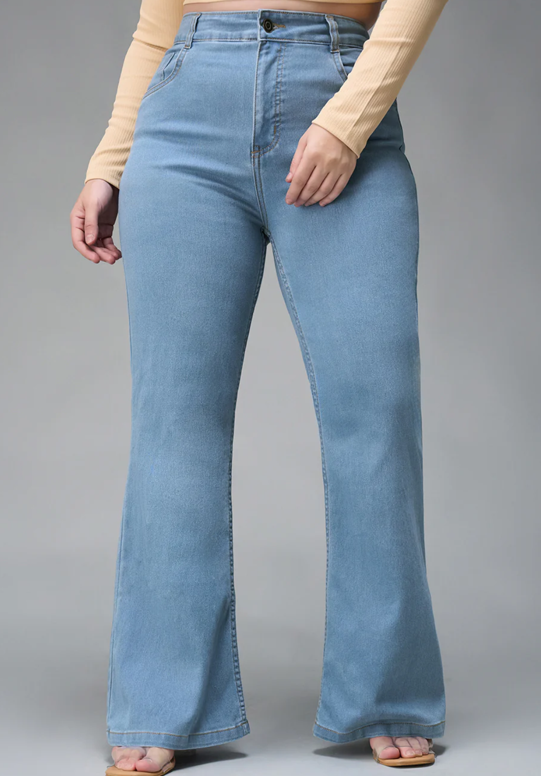 Light blue flared jeans worn by a person on a gray background
