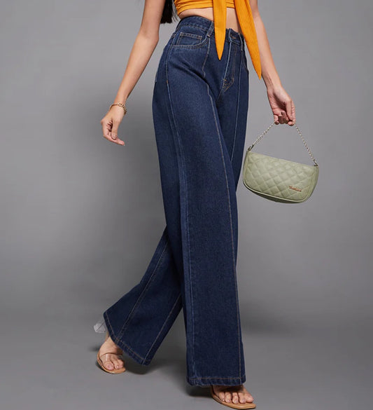 Person wearing blue jeans and holding a green handbag against a gray background
