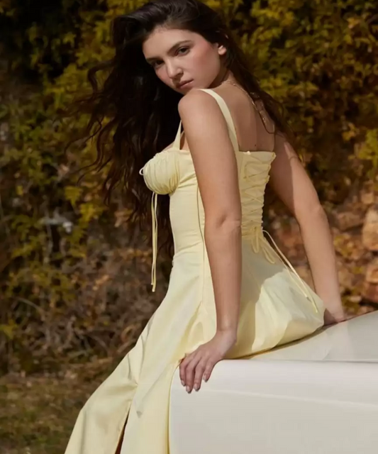 Woman in a yellow dress sitting outdoors with a blurred natural background