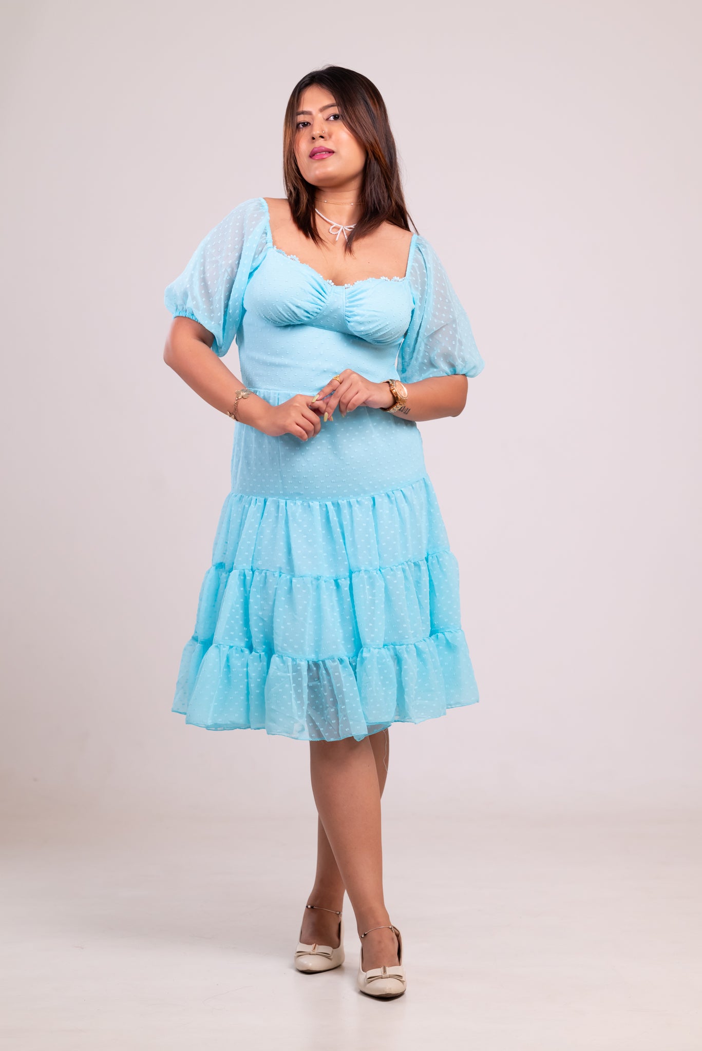 Woman wearing a light blue dress with sheer sleeves against a plain background