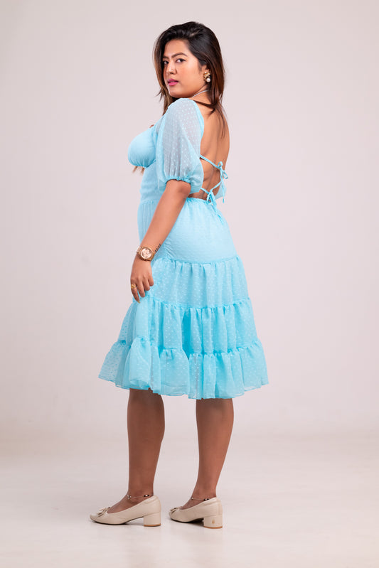 Woman wearing a light blue dress with ruffled layers on a plain background