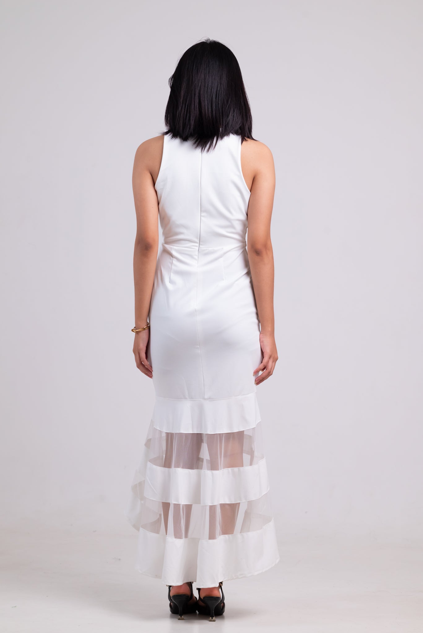 Woman wearing a white dress with sheer overlay on a plain background