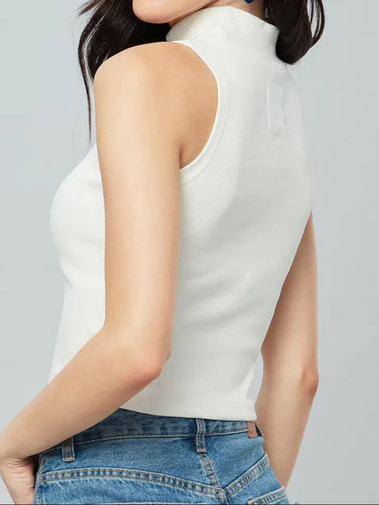 Woman wearing a white sleeveless top and blue jeans with sunglasses on her head against a gray background