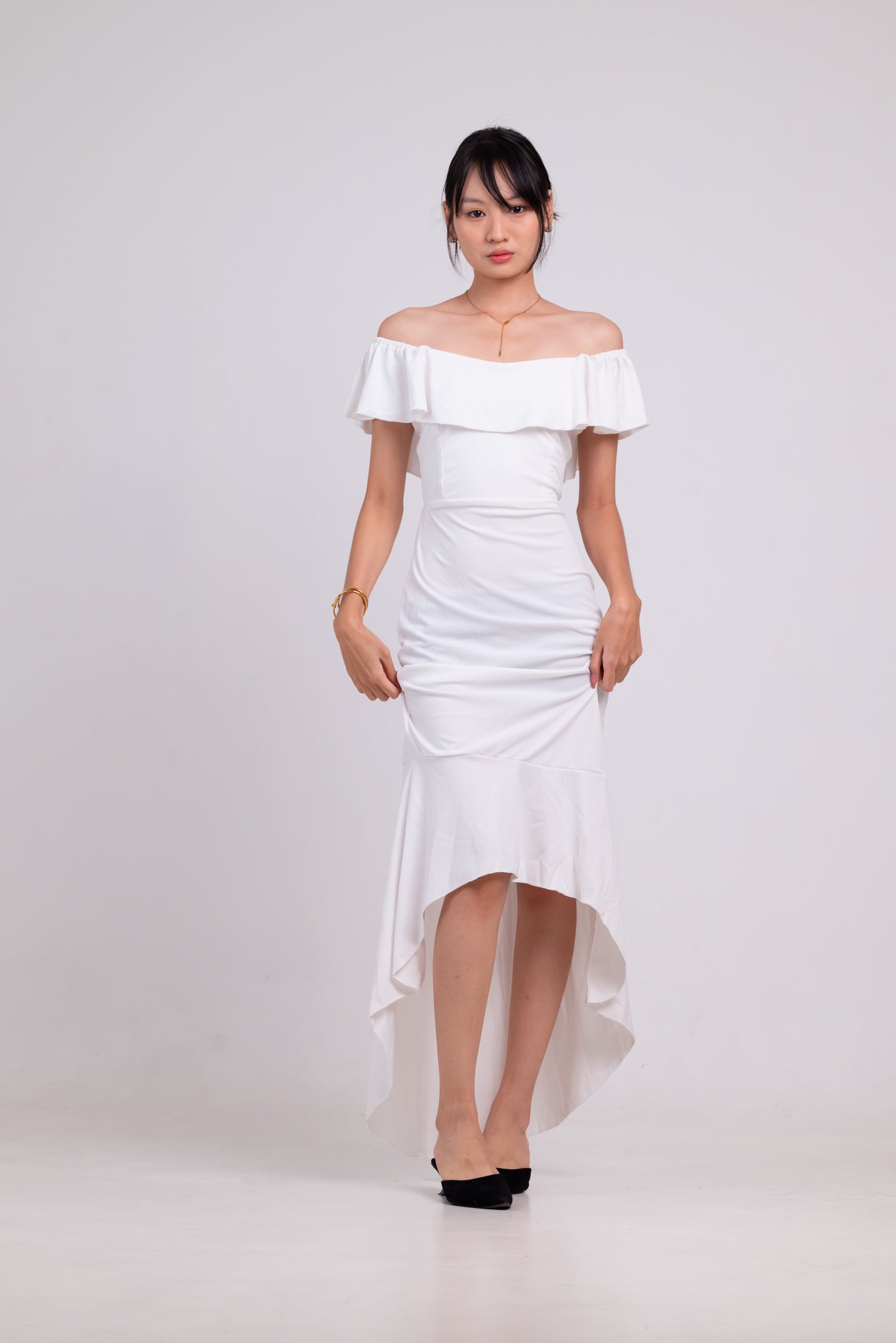 Woman wearing a white off-shoulder dress on a plain background