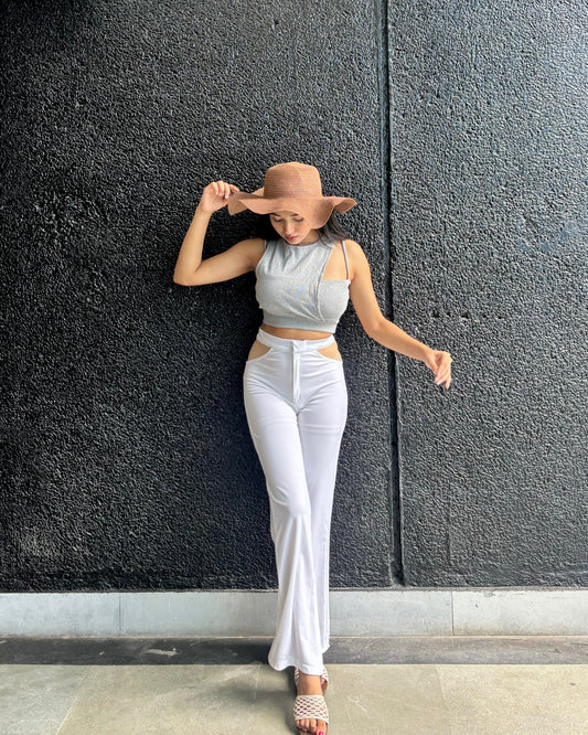 Woman wearing a light gray top and white pants against a dark textured wall.