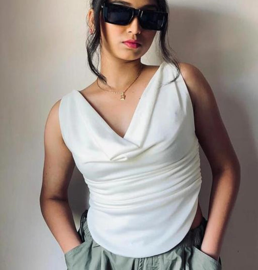 Woman wearing a white sleeveless top and sunglasses against a plain background