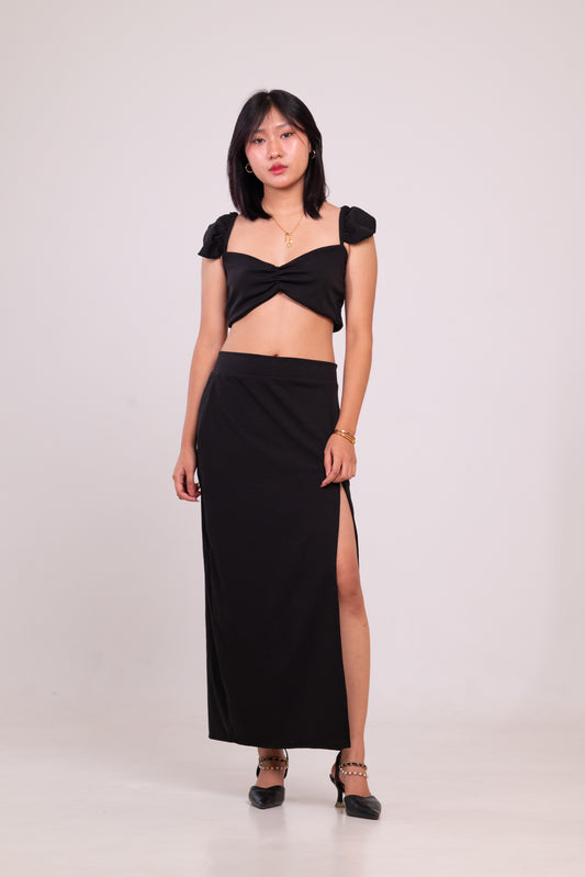 Woman wearing a black outfit with a top and long skirt on a white background