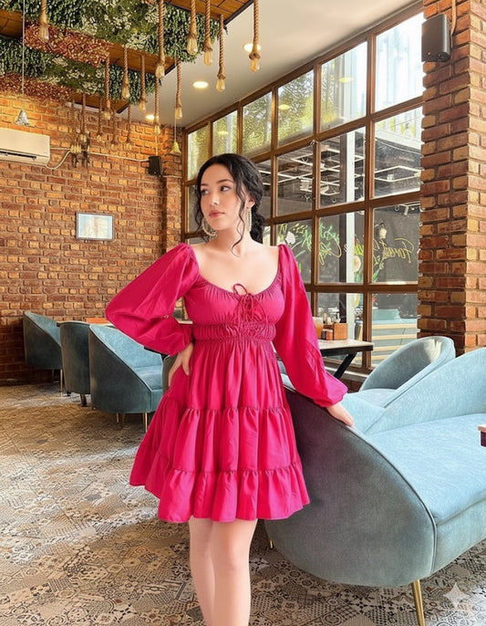 Woman in a pink dress standing in a modern interior setting with brick walls and large windows.