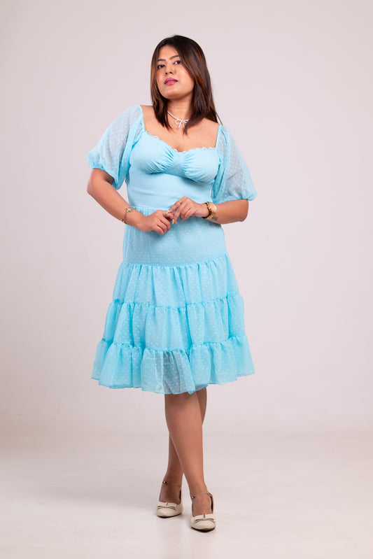 Woman wearing a light blue dress with sheer sleeves against a plain background