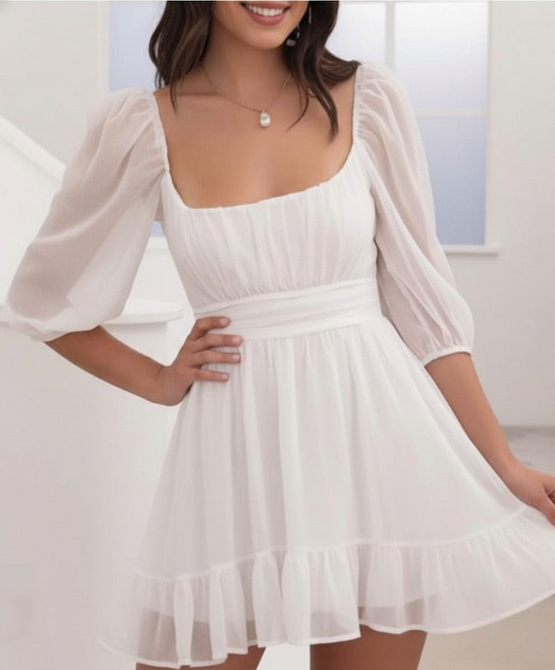 Woman wearing a white dress with sheer sleeves in a minimal indoor setting