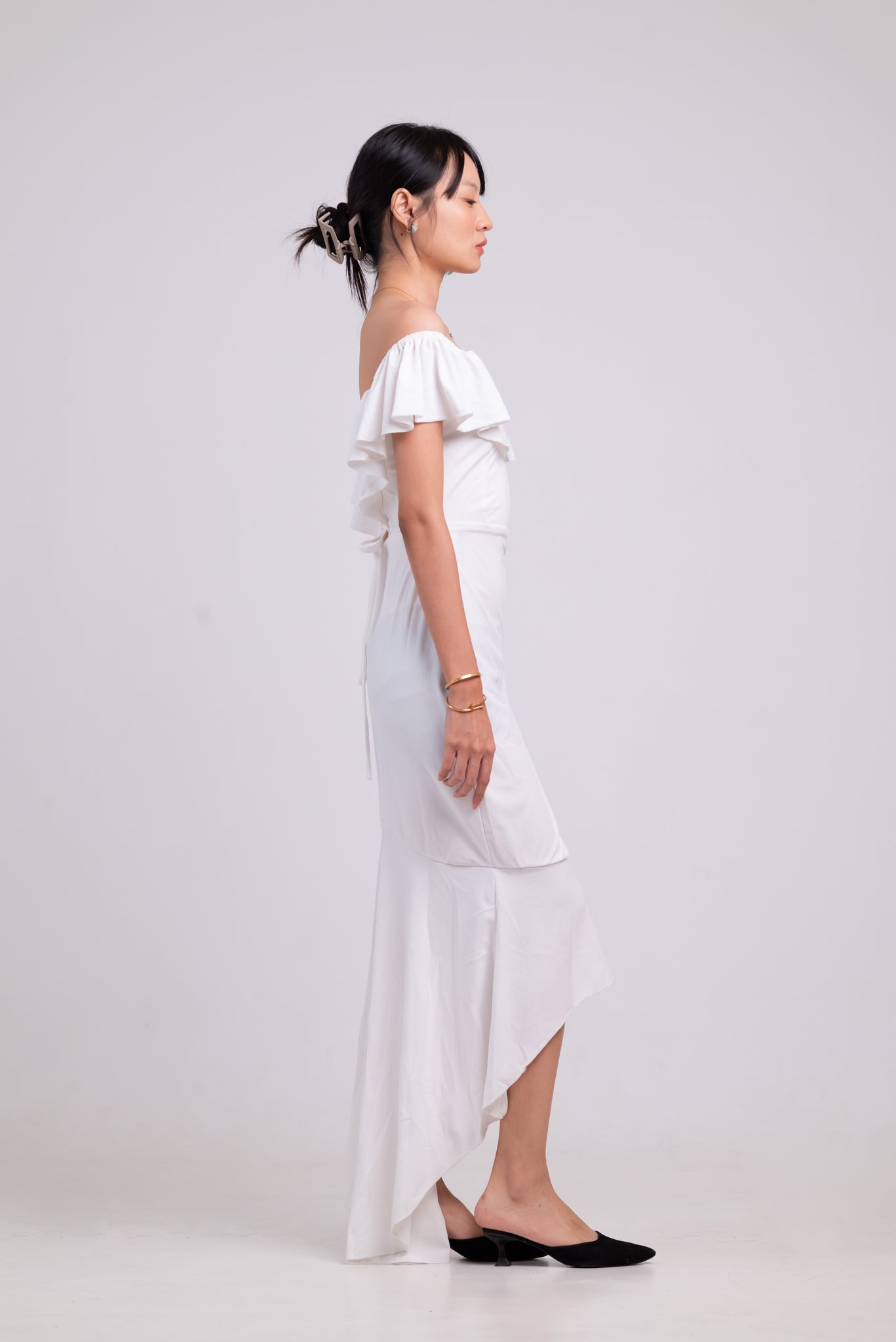 Woman wearing a white off-shoulder dress with a high-low hem on a plain background